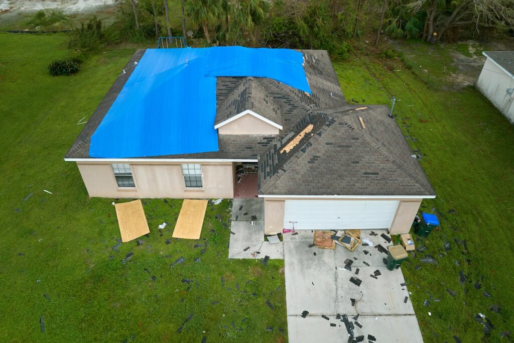 Top view of leaking house roof covered with protective tarp sheets against rain water leaks until replacement of asphalt shingles. 