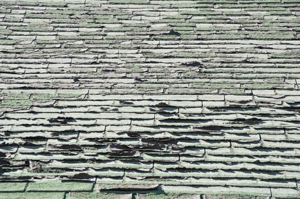 sun damaged old roof with peeling and curling composition shingles