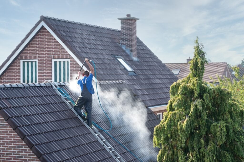 Cleaner with pressure washer at roof of house cleaning the roof tiles, removing moss and weed