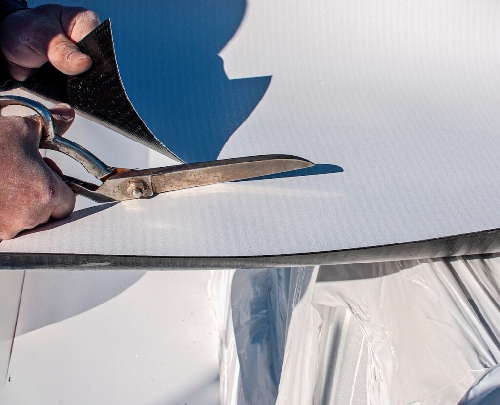 Construction worker cuts with large scissors a TPO polyolefin sheet to be applied for waterproofing a terrace of a new building