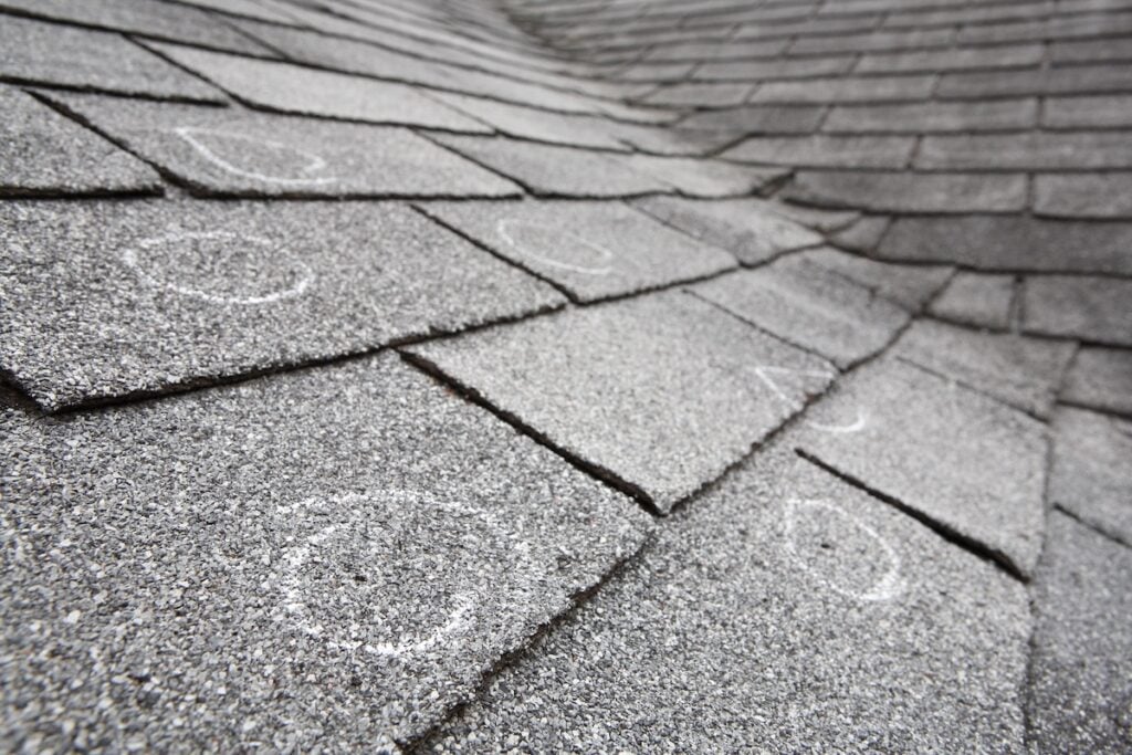 Old roof with hail damaged shingles, chalk circles mark the damage.