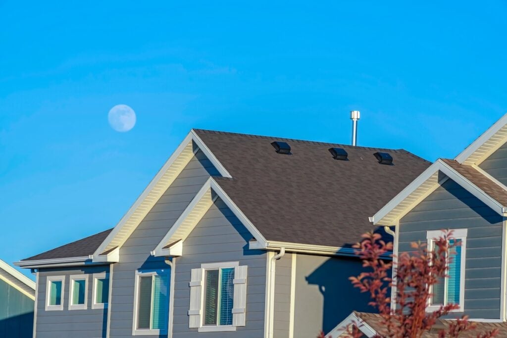 Sunlit home with dark pitched roof over horizontal gray wall siding and windows