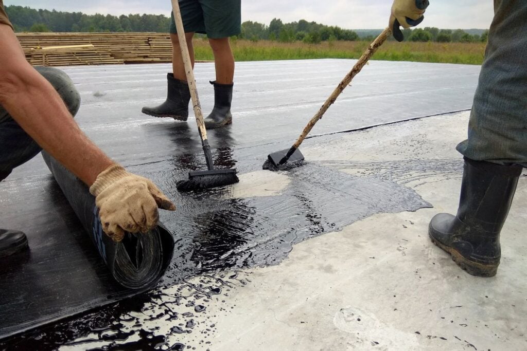 Roofer worker painting bitumen praimer at concrete surface by the roller brush Waterproofing