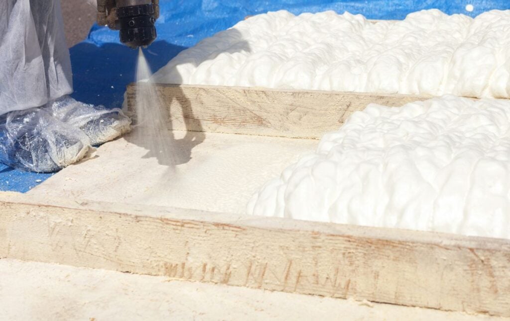 Technician dressed in a protective white uniform spraying foam insulation using Plural Component Spray Gun