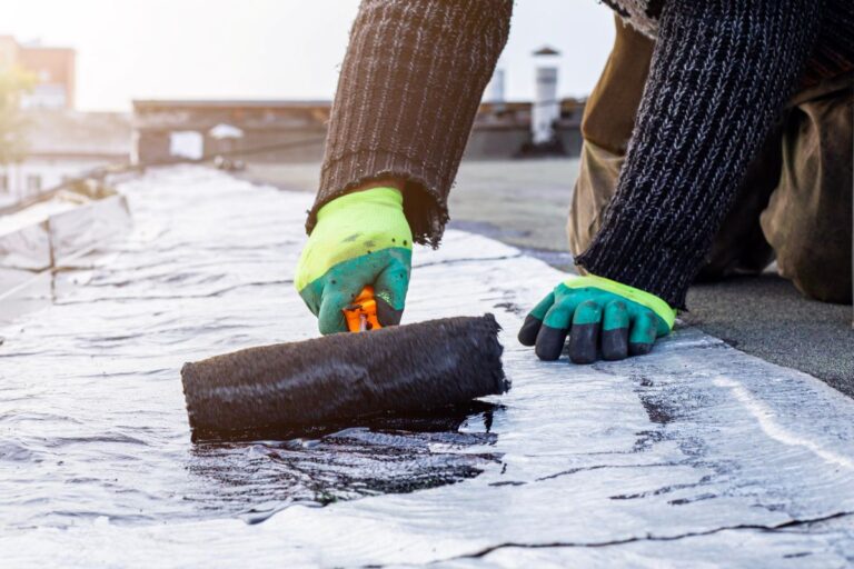 worker treats a roof with bitumen primer before applying rolled asphalt