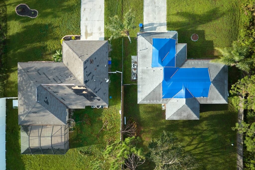 Top view of leaking house roof covered with protective tarp sheets against rain water leaks until replacement of asphalt shingles.