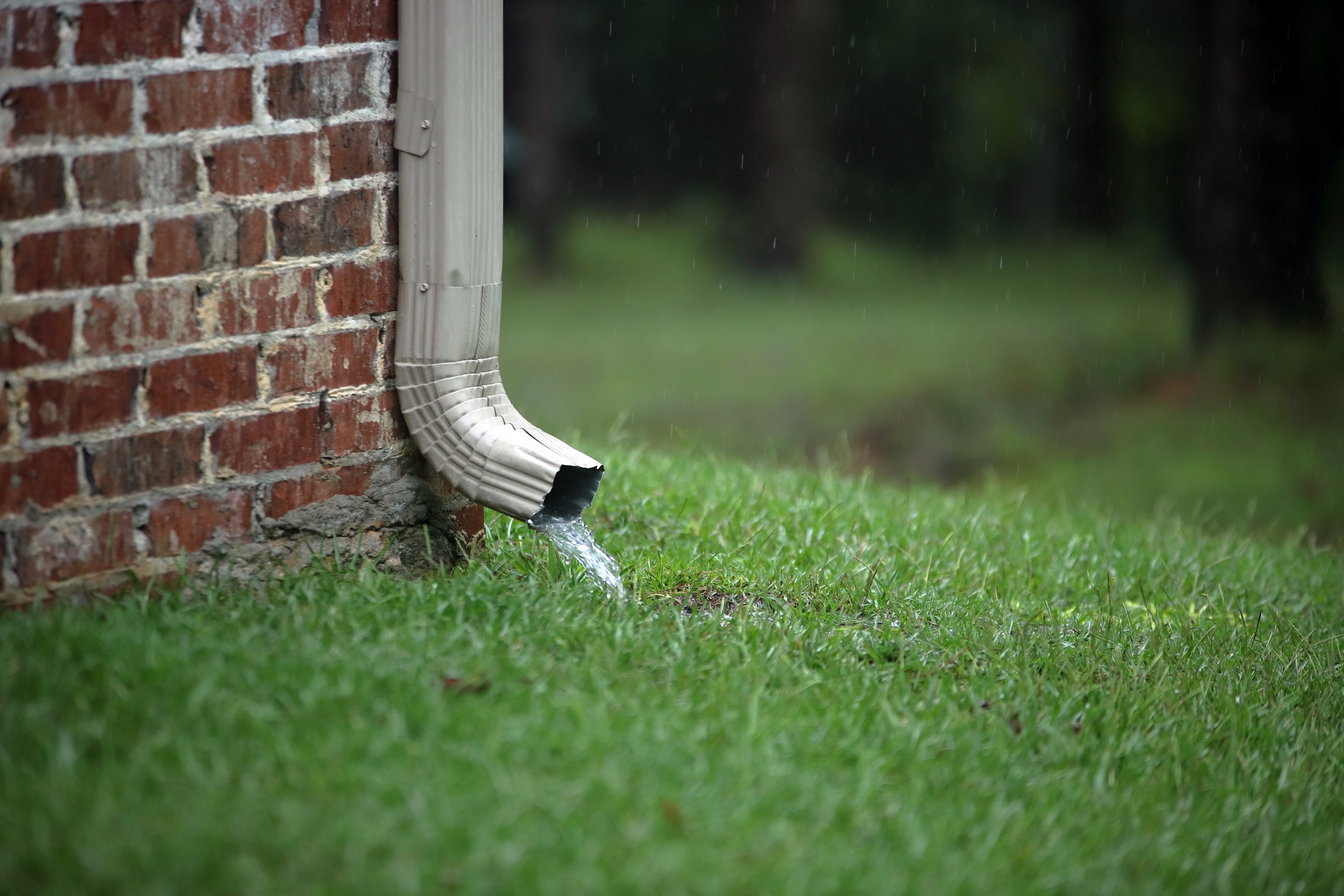 Working gutter on a brick house with flowing water into the grass during rain storm
