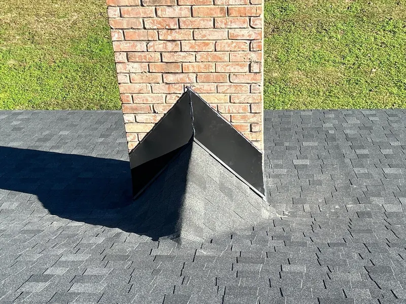 Chimney cricket and dark flashing where a brick chimney meets a gray shingle roof