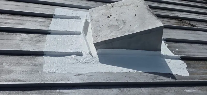 White sealing around a raised roof curb on a ribbed metal roof