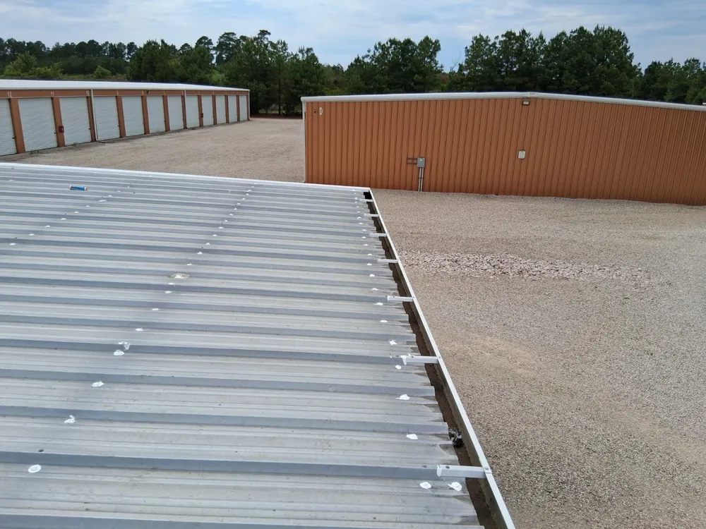 Ribbed metal roof with white sealant around fasteners beside storage buildings