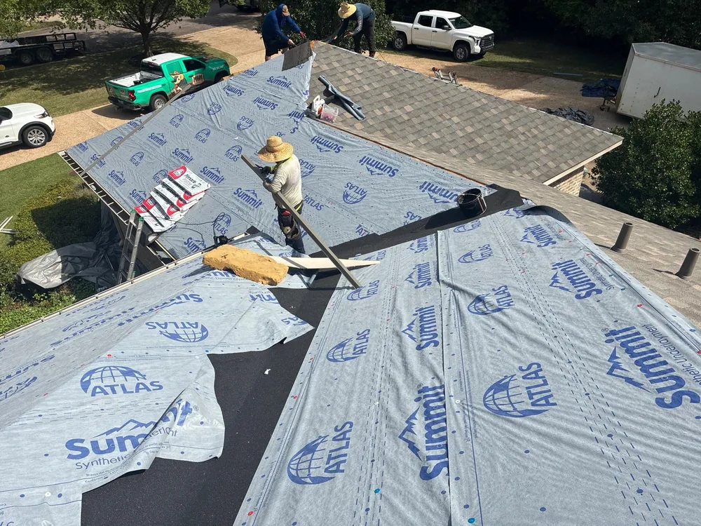 Roofers installing shingles beside synthetic roof underlayment on a residential roof